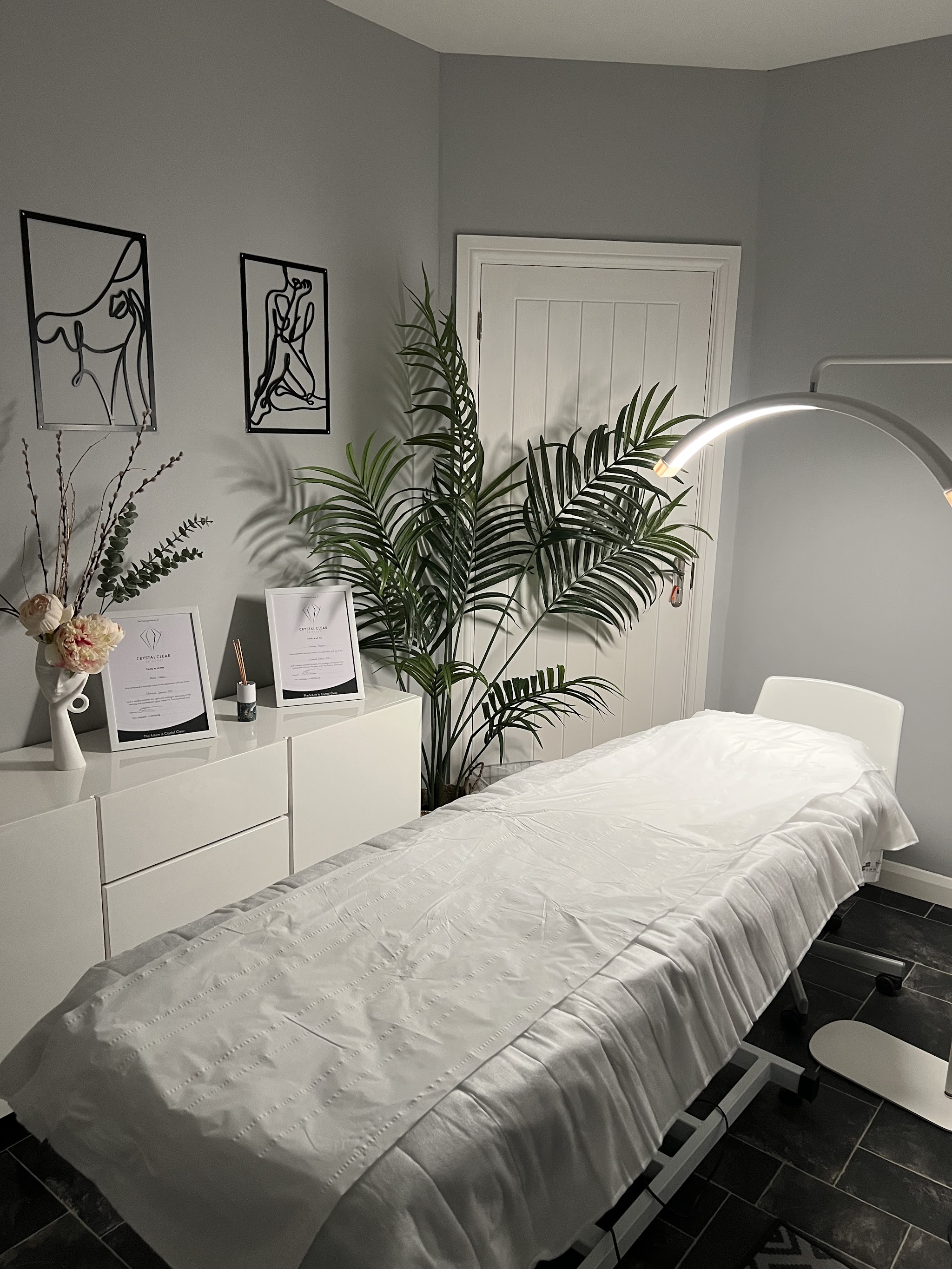 A treatment room at Cristina's Beauty Secrets with a white treatment bed, framed certificates and line-art prints