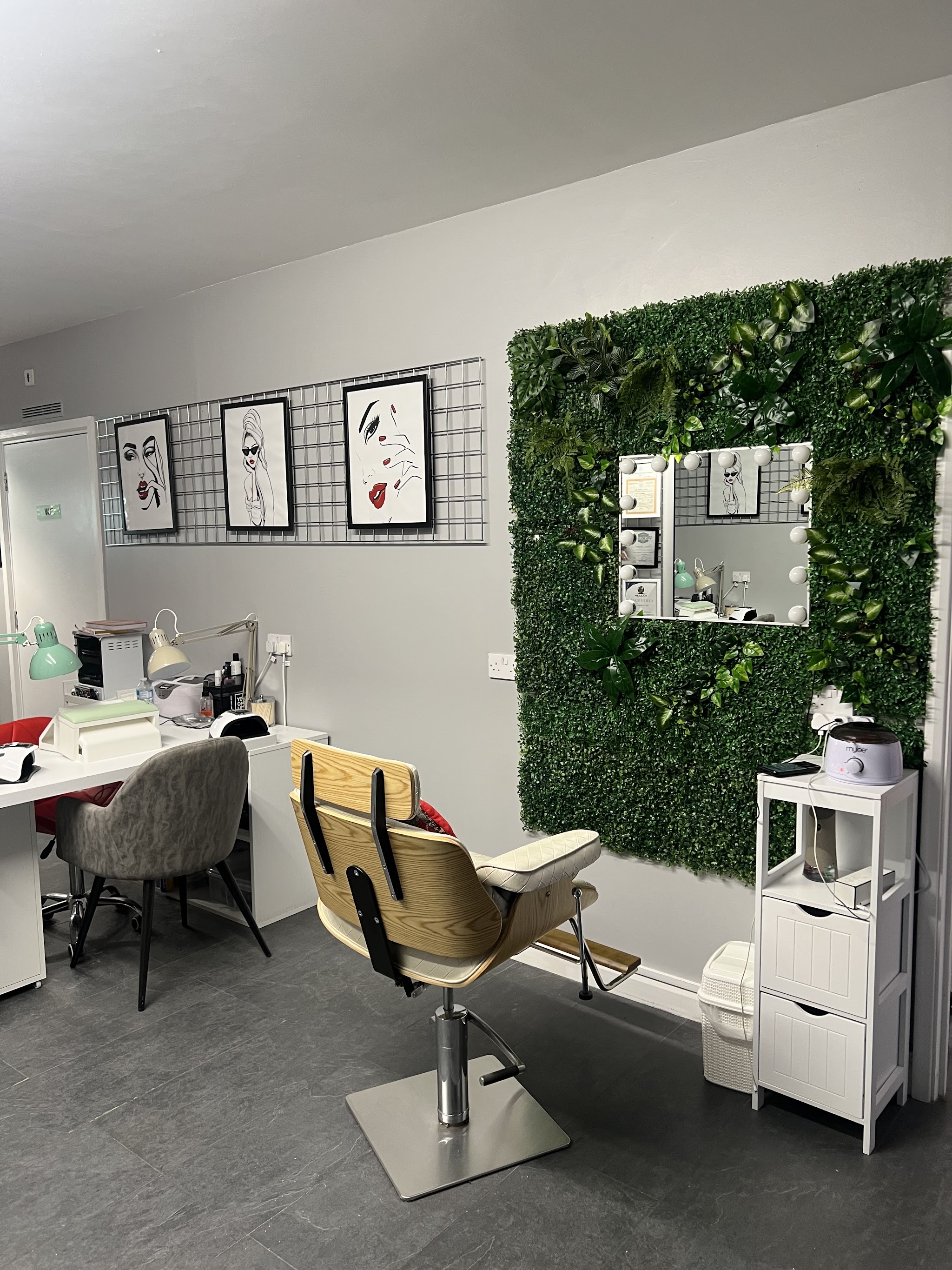 The salon floor with a cream treatment chair, a lit mirror in a green foliage wall and a nail desk