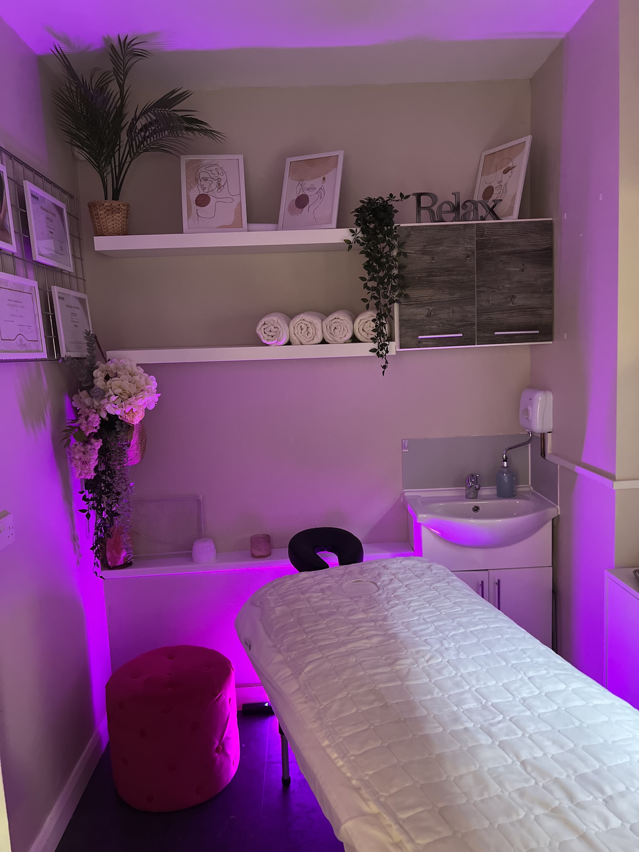 A treatment room lit in purple, with towels on the shelves and a Relax sign