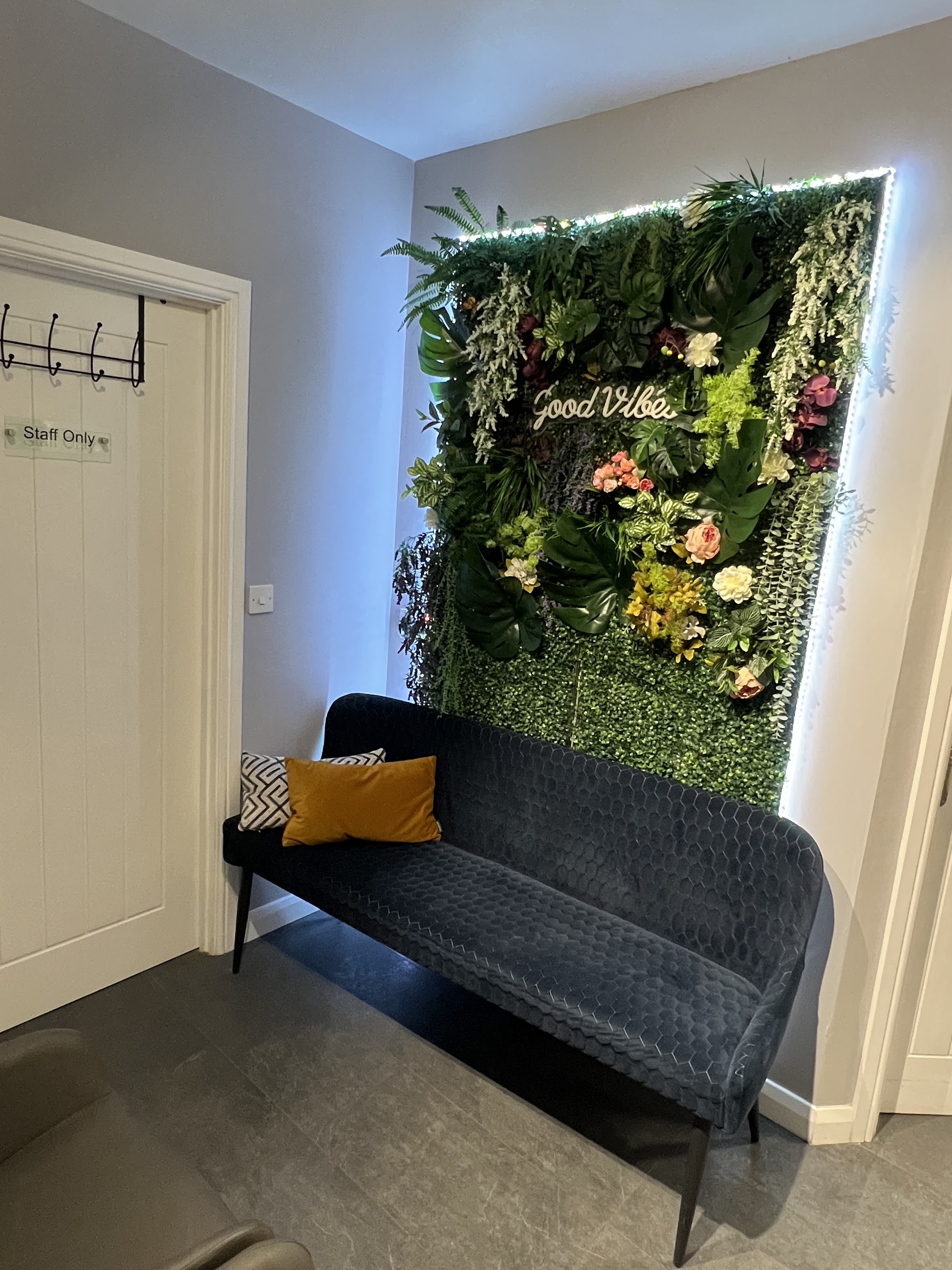 The waiting area at Cristina's Beauty Secrets: a navy velvet bench under a lit flower wall with a Good Vibes neon sign