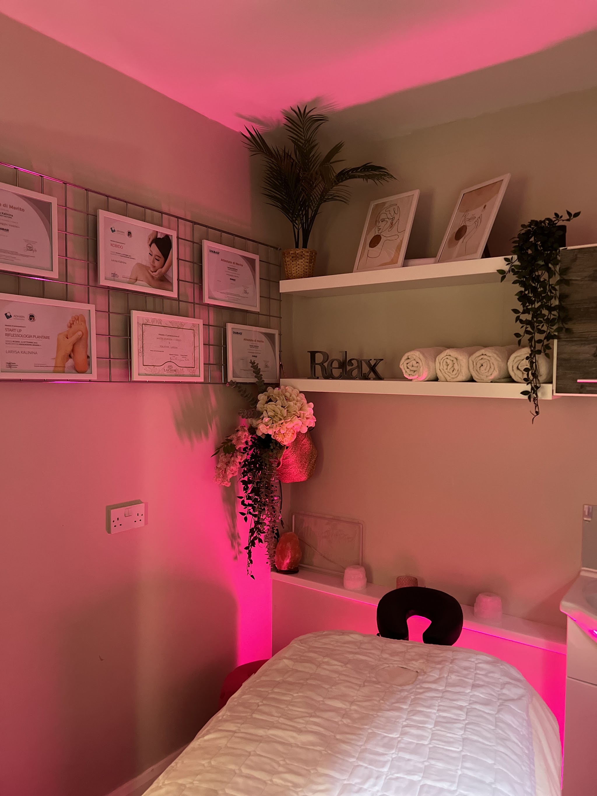 A treatment room under pink light with a wall of framed certificates
